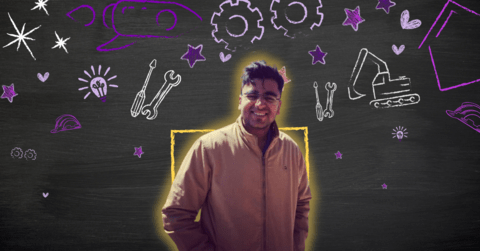 Bhagya smiling in front of a black board with white and purple engineering themed chalk drawings on it.